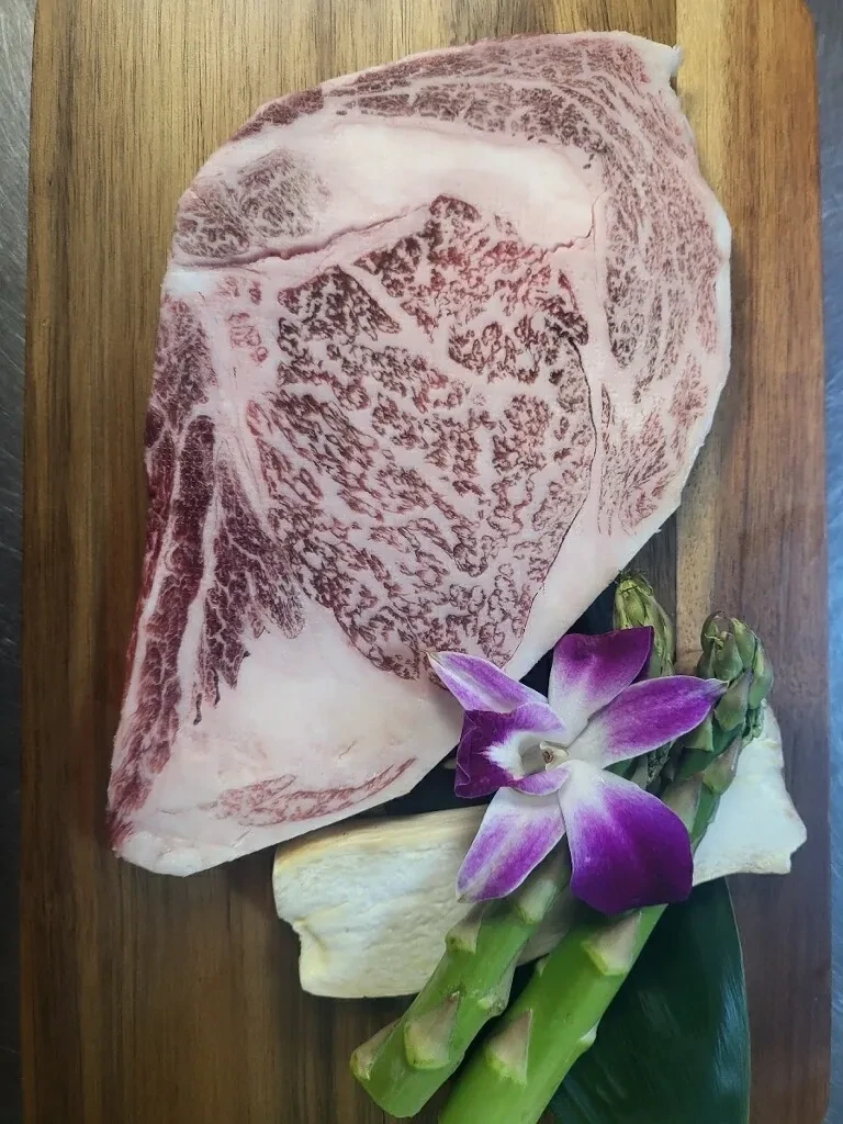 Premium Japanese wagyu ribeye with orchid and asparagus on wooden board