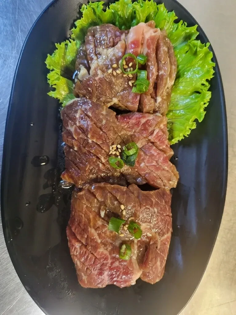 Grilled beef short rib slices with sesame and green onion on black plate