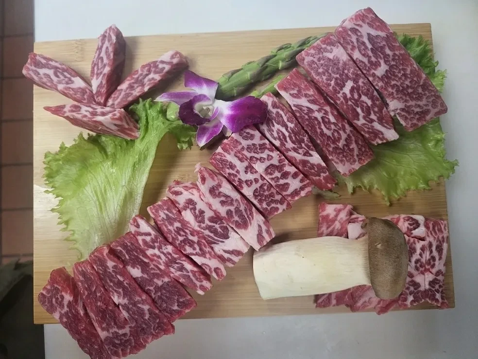 Sliced wagyu short rib and beef cuts arranged on bamboo board with orchid garnish